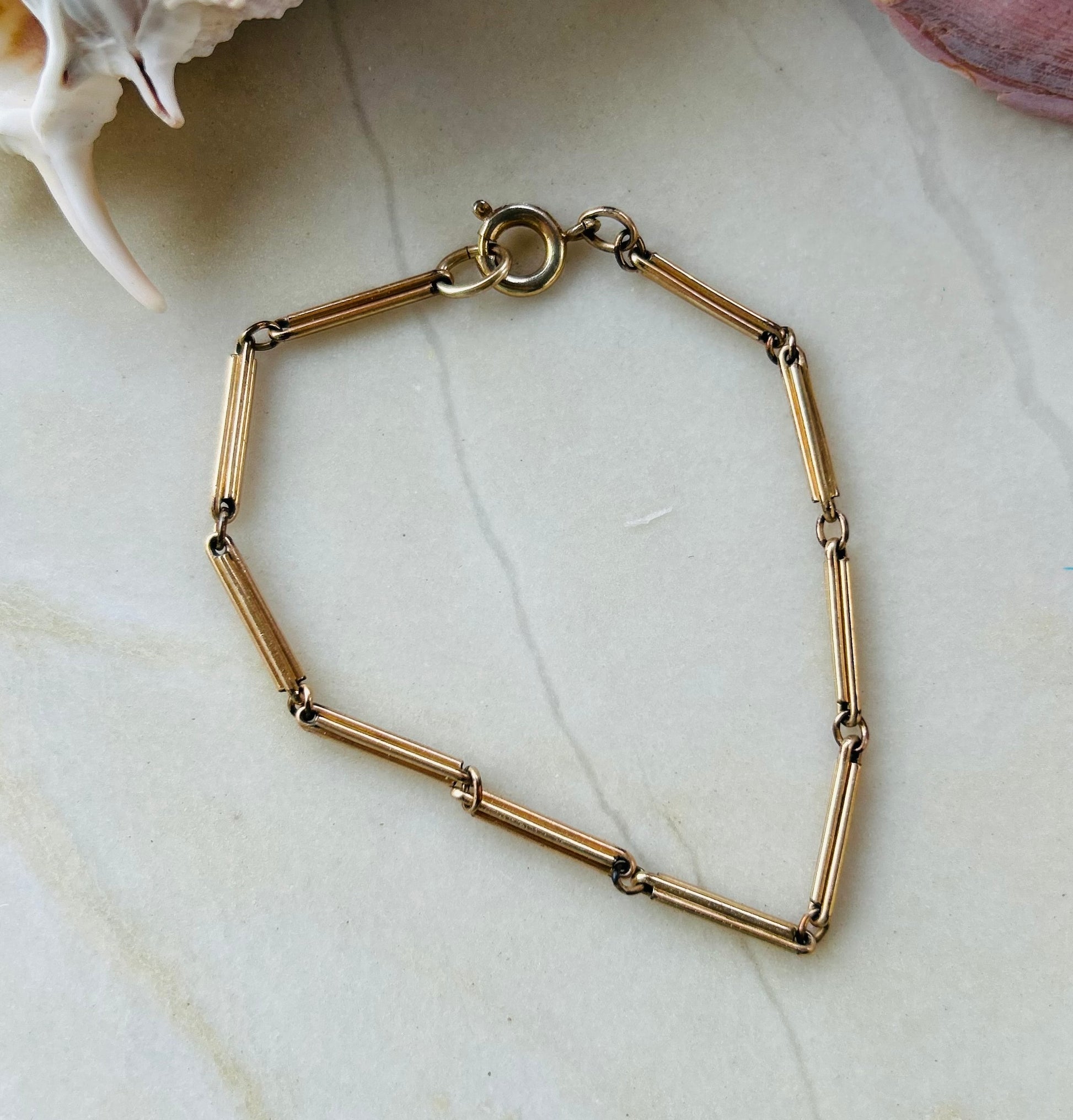 Gold bracelet on a light marble surface with a shell in the background